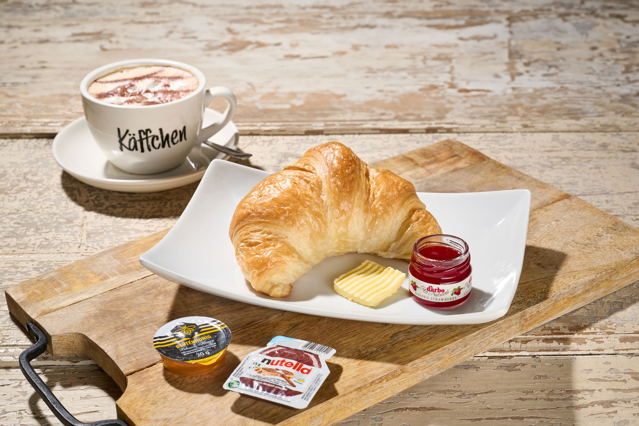 Schäfers süßes Glück Buttriges Croissant mit Butter, Erdbeermarmelade, Honig, Nutella und einer Tasse Cappuccino auf Holzbrett
