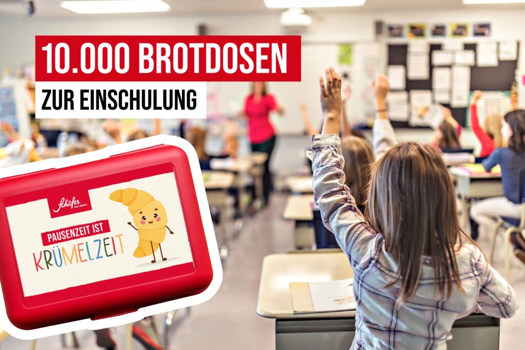 Schulkinder im Klassenzimmer heben die Hände; im Vordergrund eine rote Brotdose mit dem Aufdruck „Pausenzeit ist Krümelzeit“ und der Einblendung „10.000 Brotdosen zur Einschulung“.