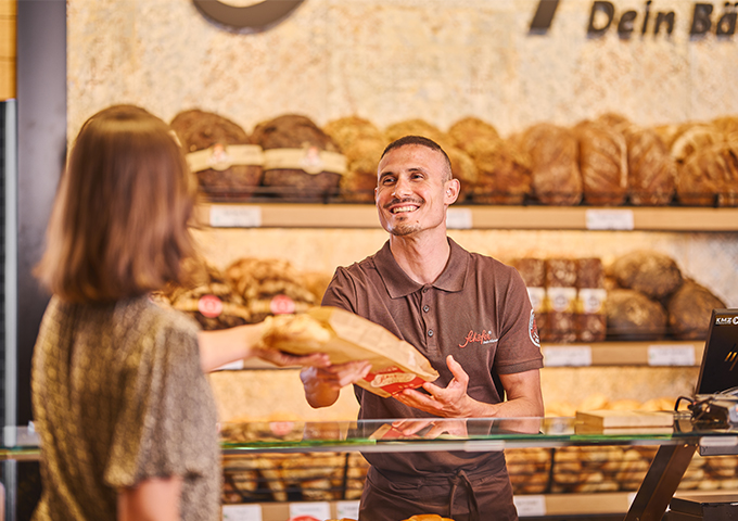 Drei Mitarbeitende einer Bäckerei in Uniform lächeln in die Kamera. 