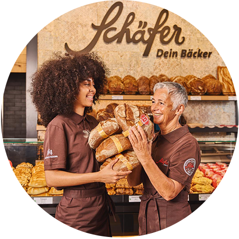 Lächelnde Bäckereifachverkäuferin reicht Brot einem Kunden im Verkaufsraum