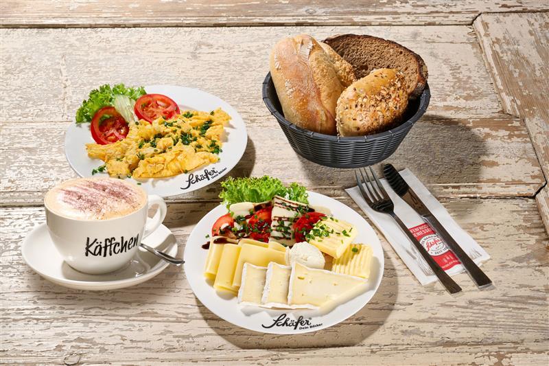 Rustikaler Teller mit Rührei, Butter, Salat und einem Körnerbrötchen auf hellem Holz